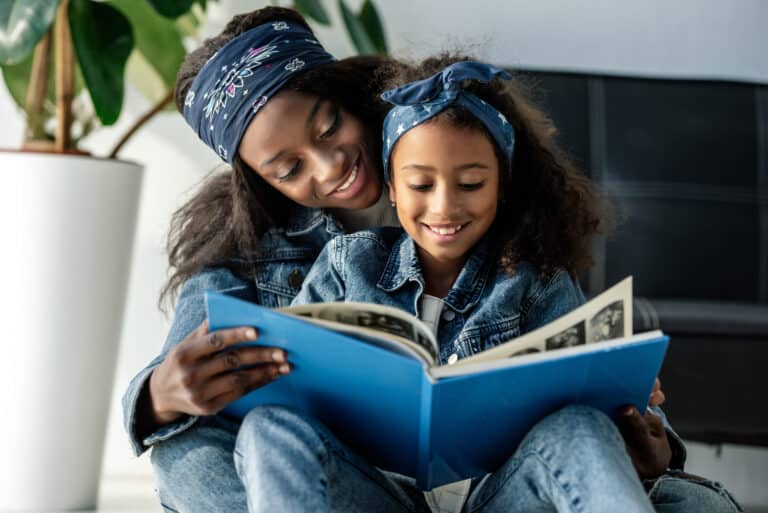 Portrait of smiling african american mother and daughter looking at family photo album at home — Photo