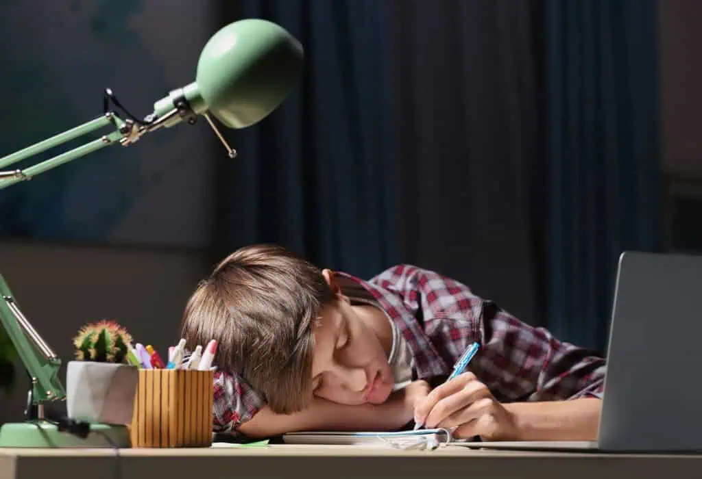 Teenager falling asleep while doing homework at table in evening