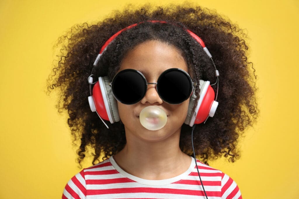 Child blows bubble gum bubble while wearing headphones