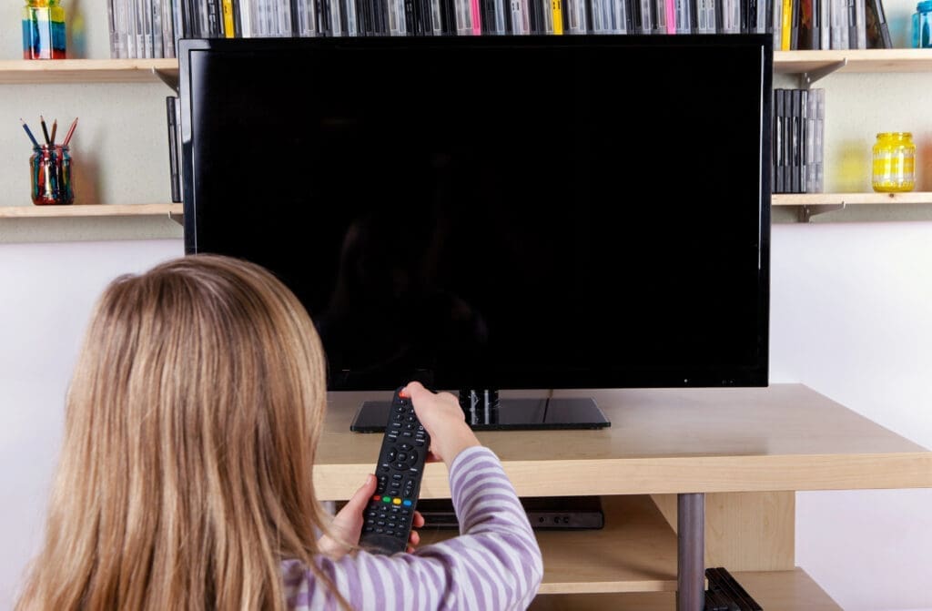 Young girl turning on or off the TV with a remote control