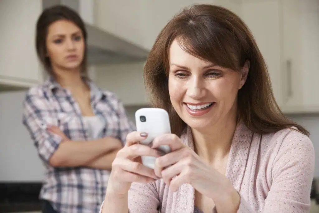 Mother Texts On Mobile Phone As Daughter Watches In Background