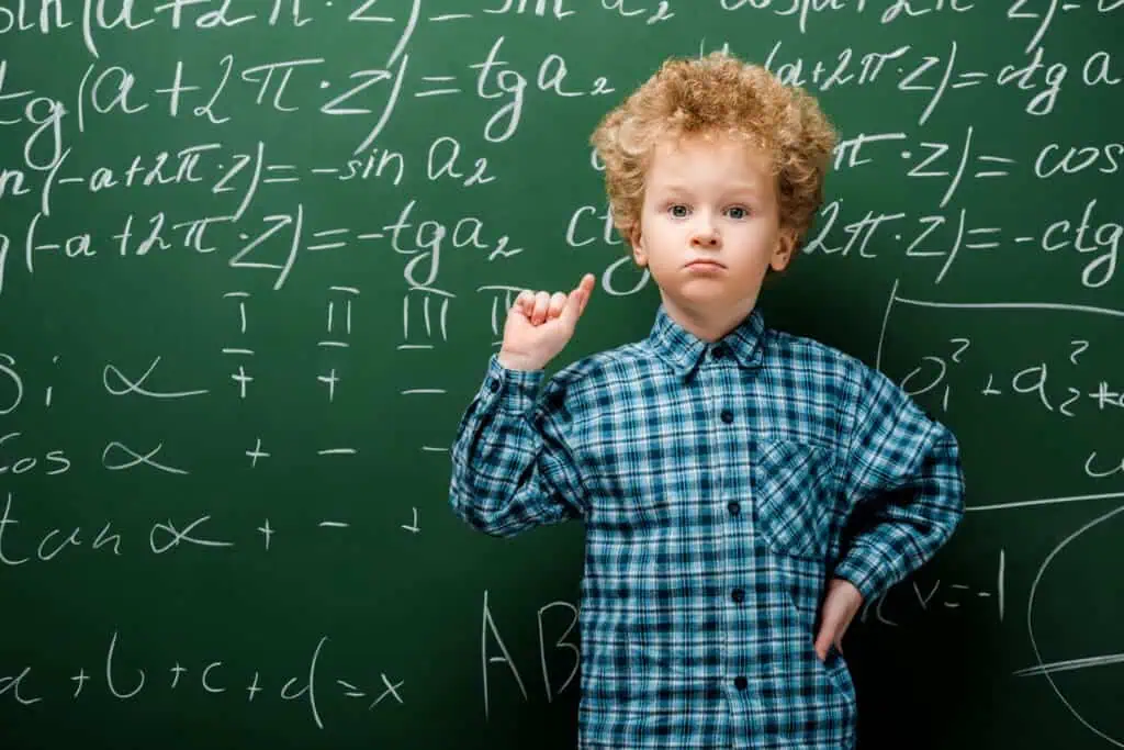 smart kid standing with hand on hip near chalkboard with mathematical formulas