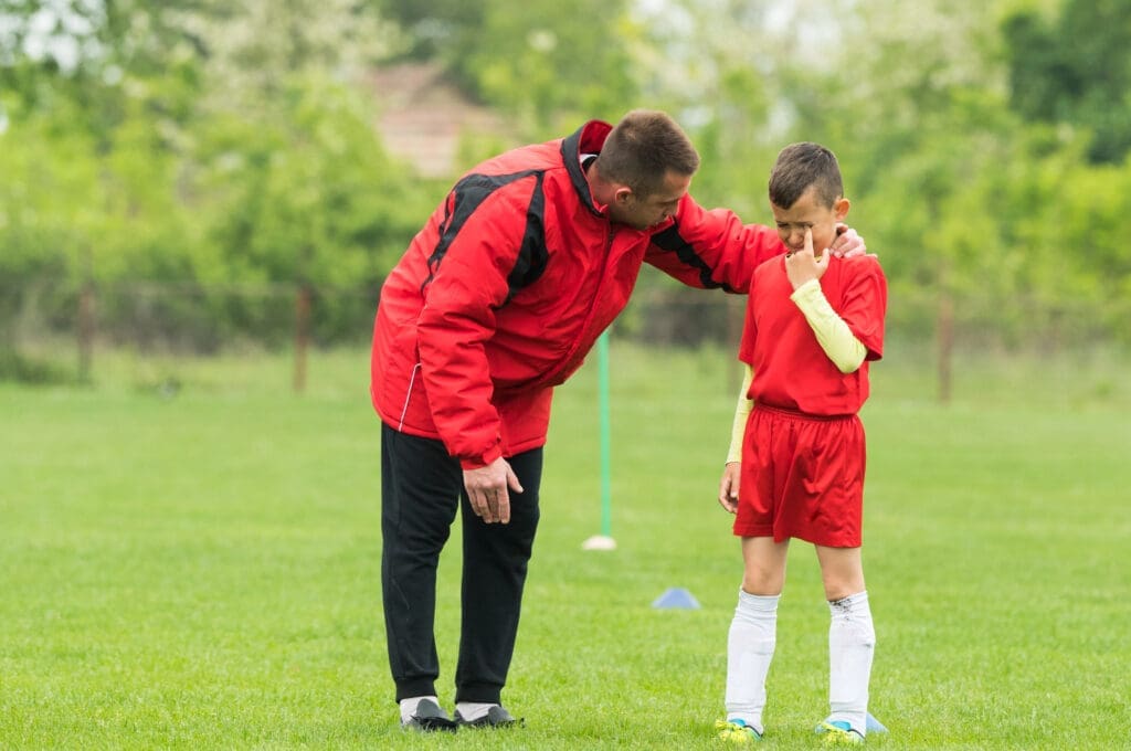 Coach comforts crying kid on soccer field