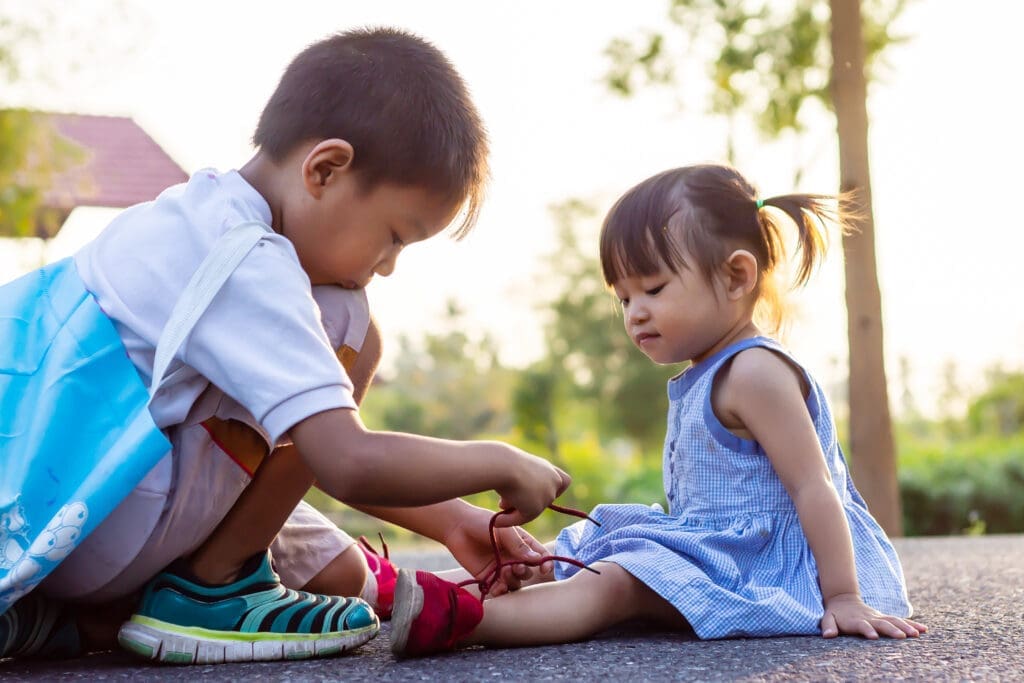 small boy helps sister tie shoes