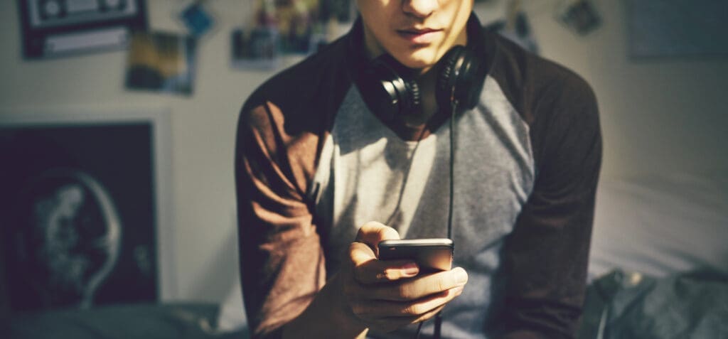 Teenage boy in a bedroom listening to music through his smartphone