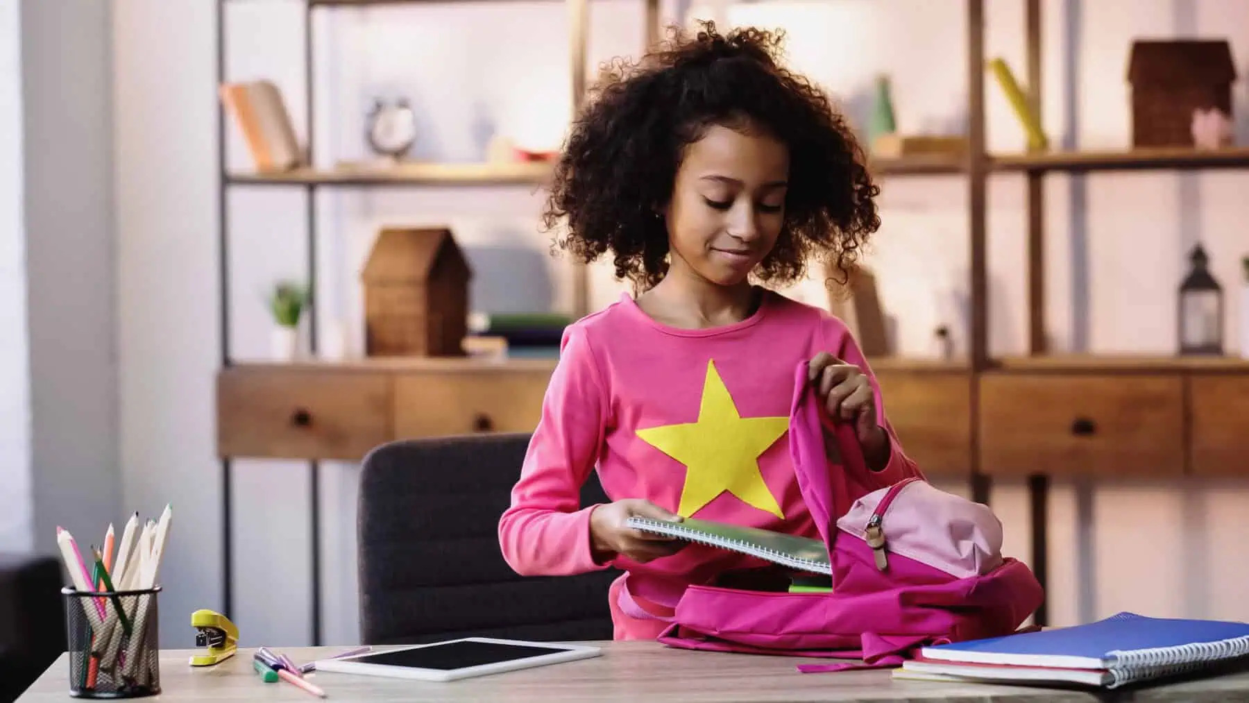 cheerful african american child putting notebook in backpack