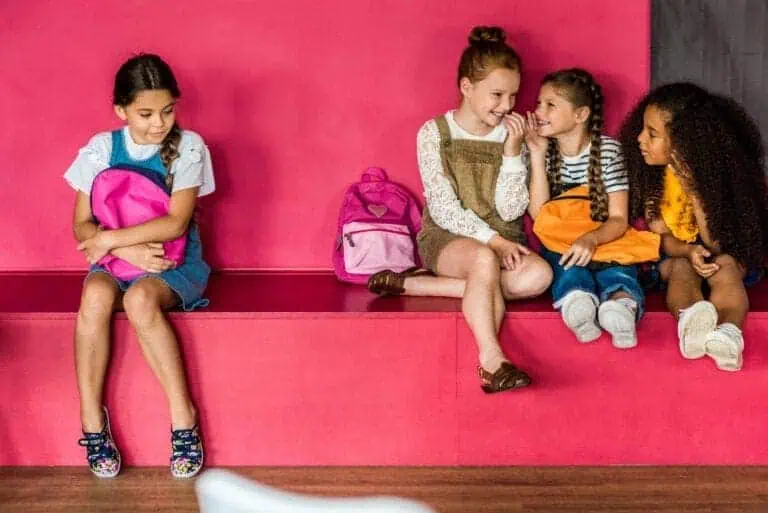 Several girls giggle and talk while another sits excluded a short distance away