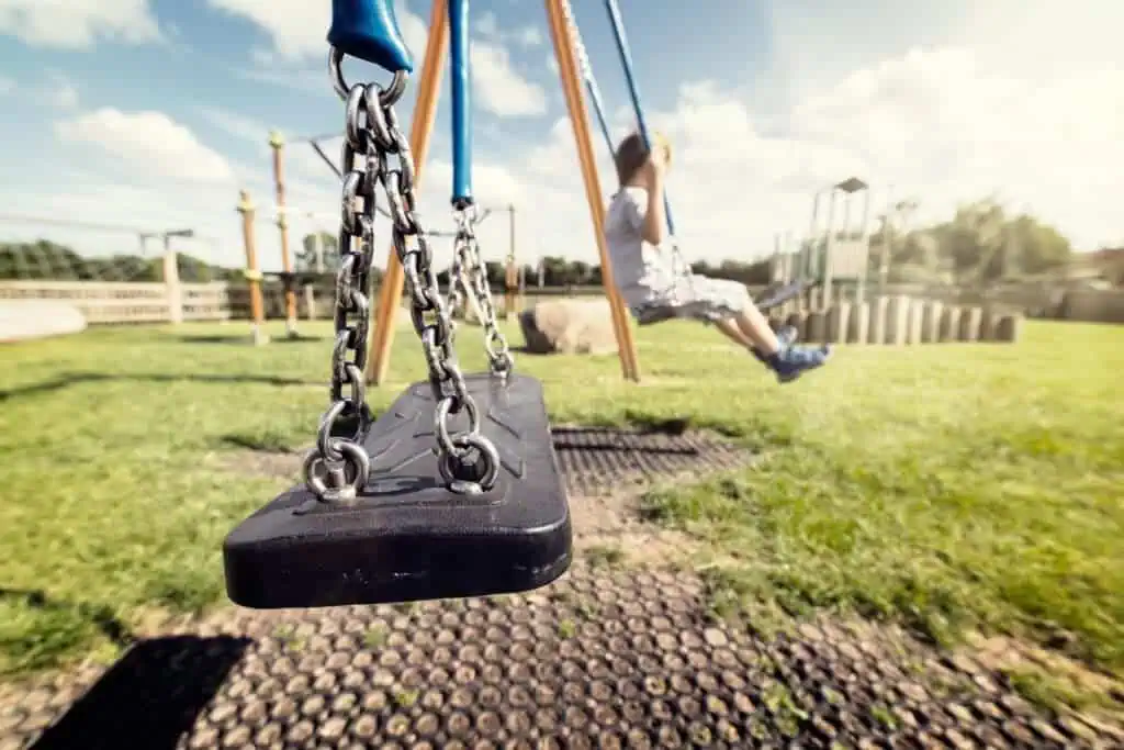 Image shows an empty swing in the foreground with a child playing in the backgroud