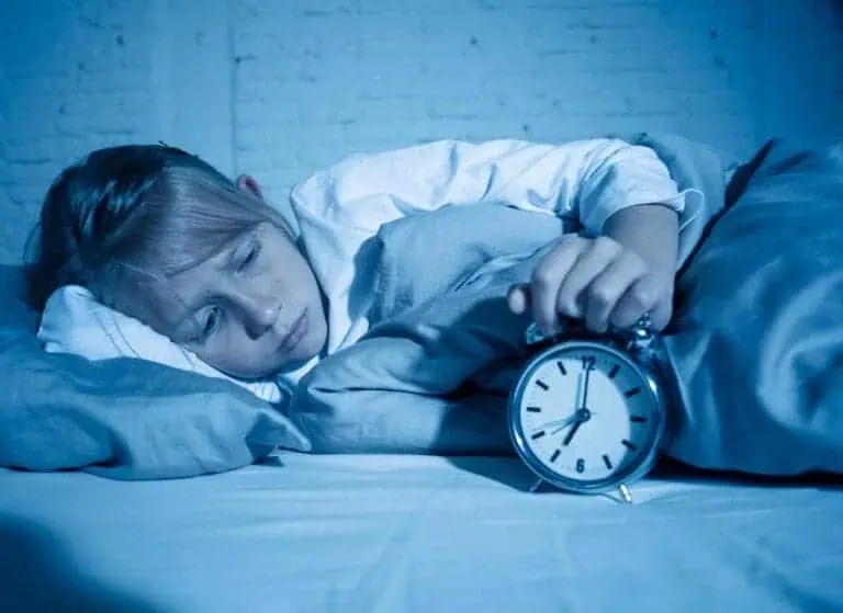Child lies awake in bed while holding alarm clock