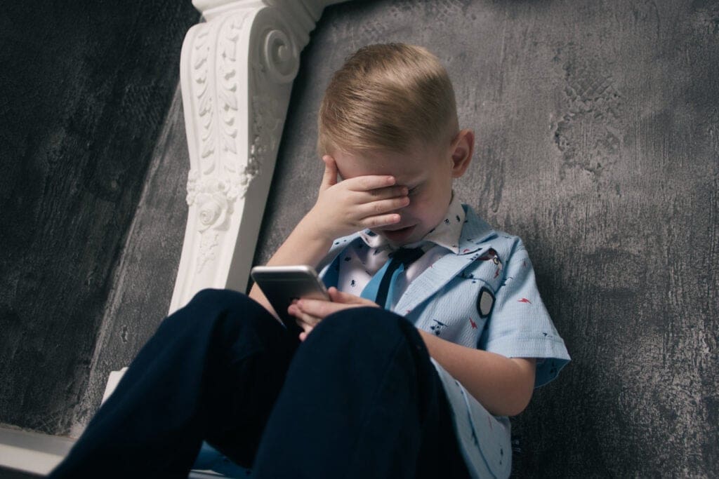 Boy hides face while looking at cell phone near wall