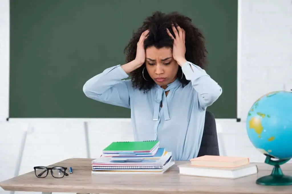 Tired teacher having headache near stationery and globe in classroom
