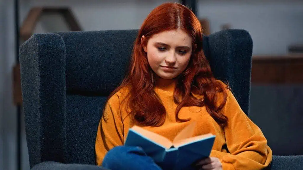 Teenager reading book on blurred foreground in armchair