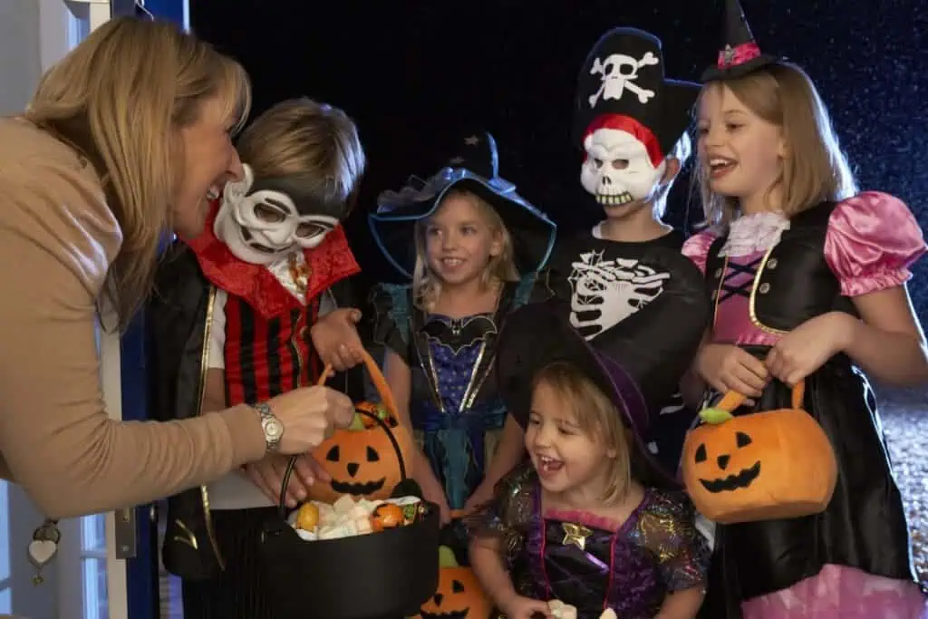 Children trick-or-treating in costumes and receiving candy in pumpkin buckets