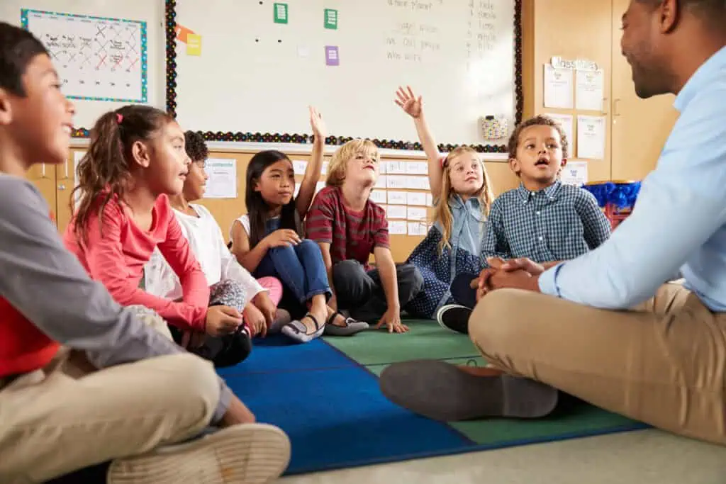 Elementary students raise hands during lesson