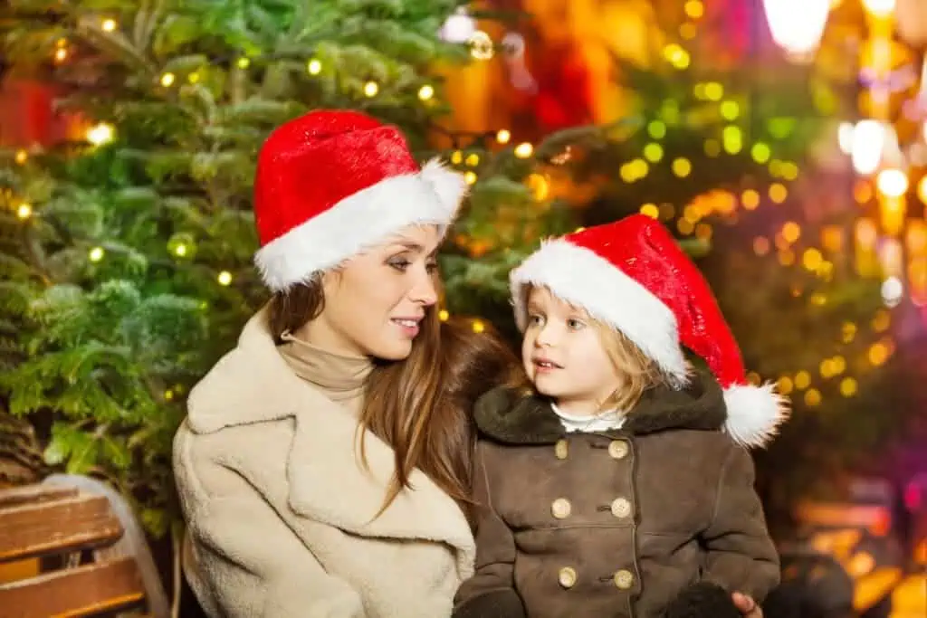 child and parent have a chat on a bench in front of Christmas trees