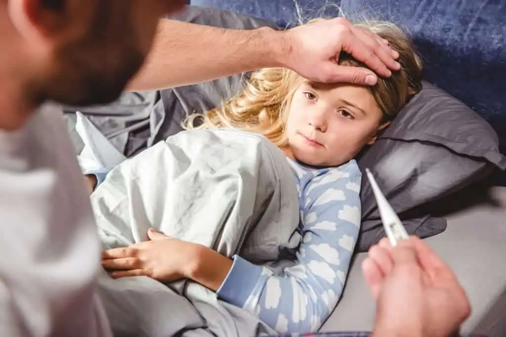 Child lies in bed sick while parent checks for fever