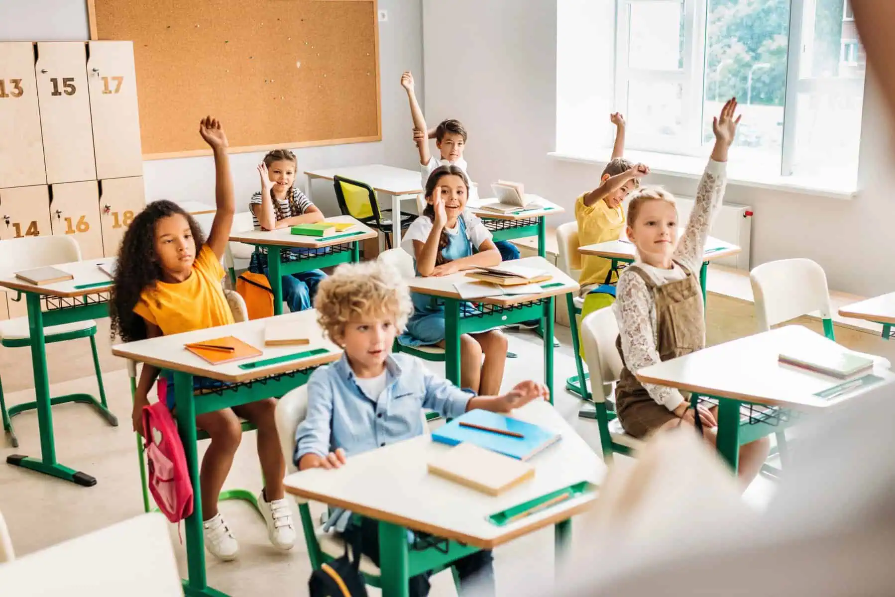 students raise hands in elementary classroom