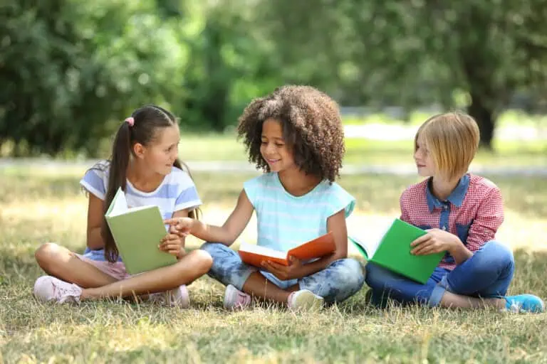 Three children reading books outside in the grass
