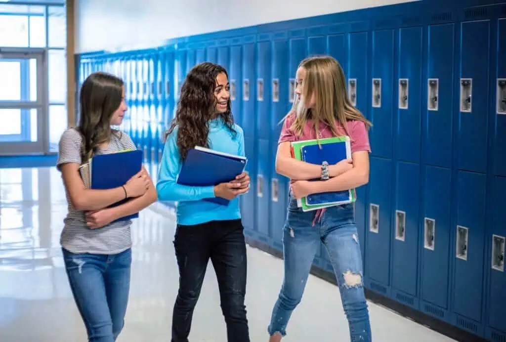 Candid photo of Three Junior High school Students talking together in a school hallway. Diverse Female school girls smiling and having fun together during a break at school