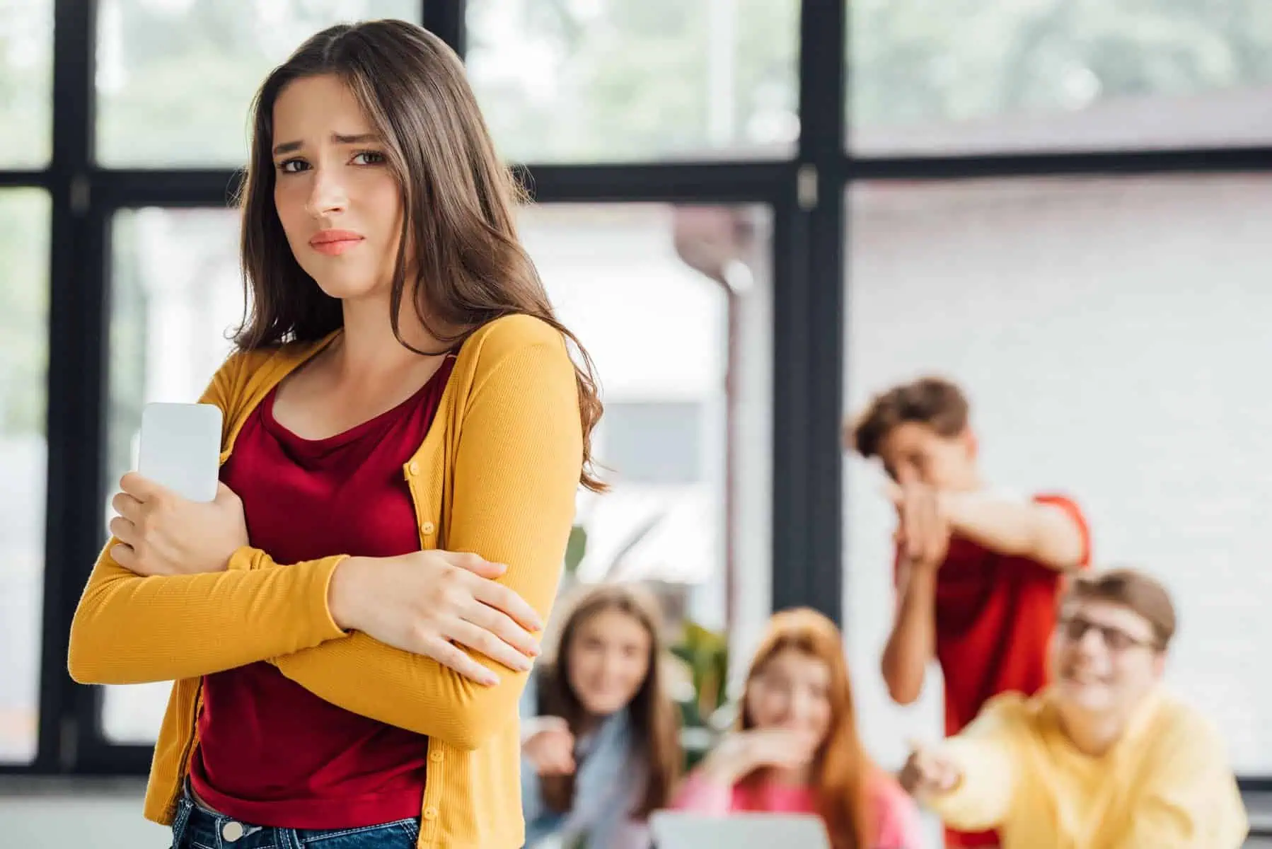 Girl is excluded as she stands away from a group of classmates mocking her