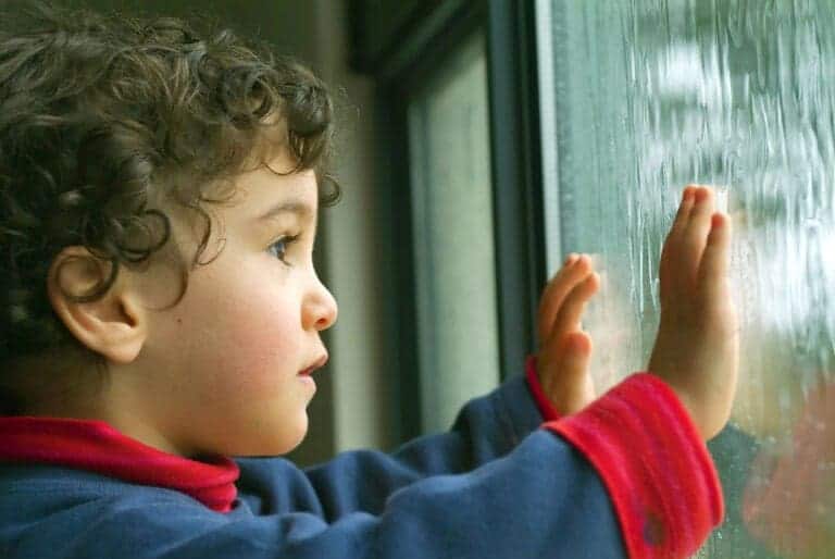 Child looks out window at rain with concerned expression