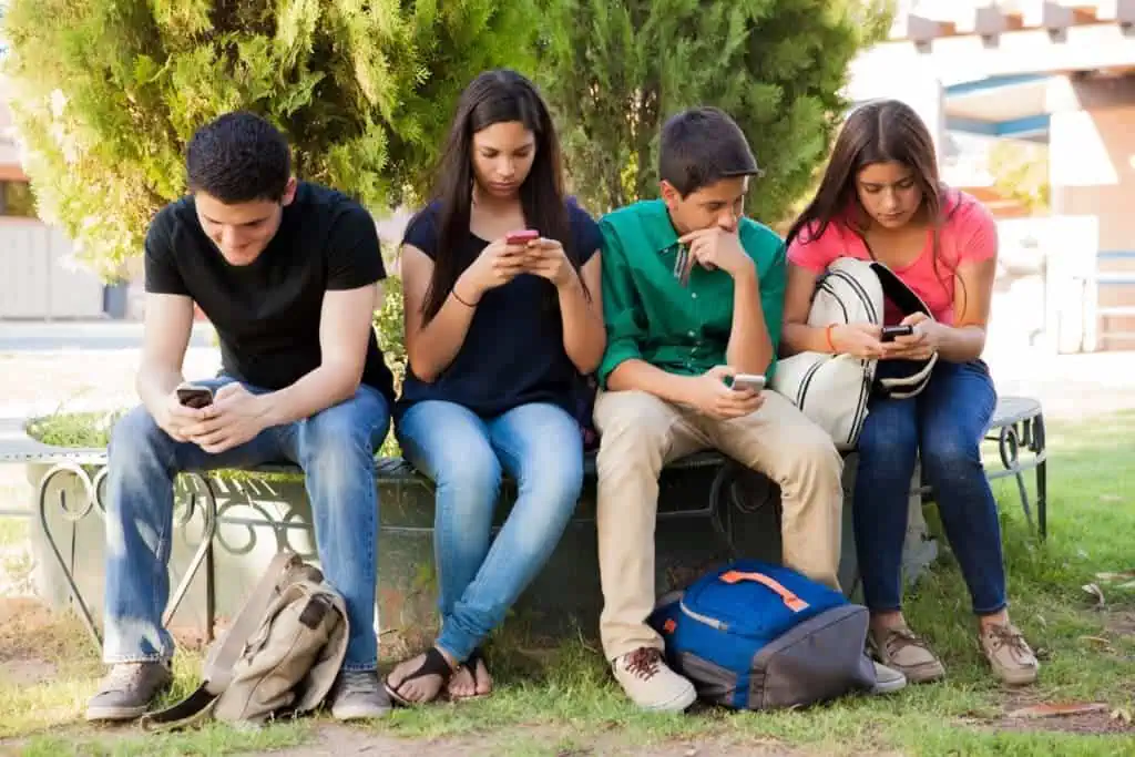 four teens sit together focusing on their smartphones