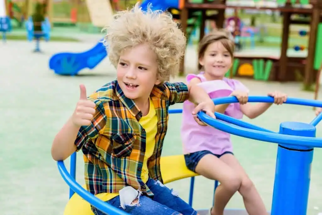 Child gives thumbs up while playing on playground