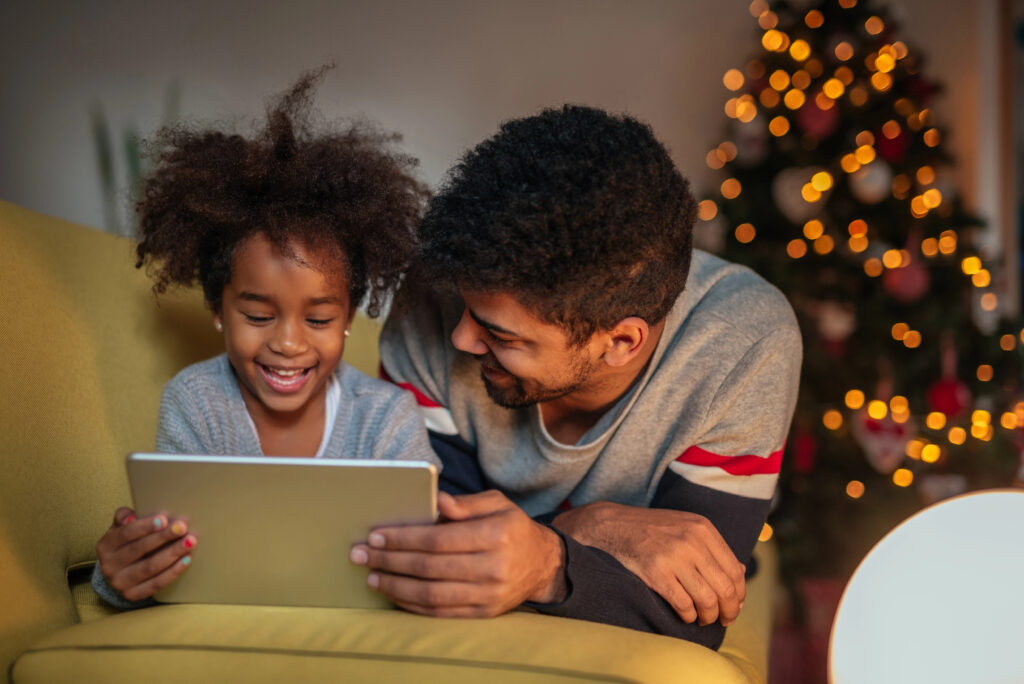 Dad and daughter try out tablet computer in front of Christmas tree