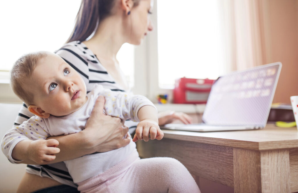 Mom checks computer while holding baby