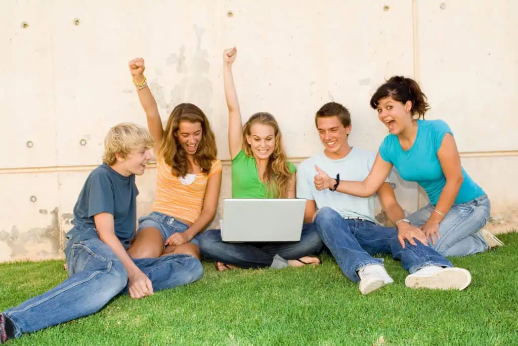 Group of teens with laptop hands raised for success or winning