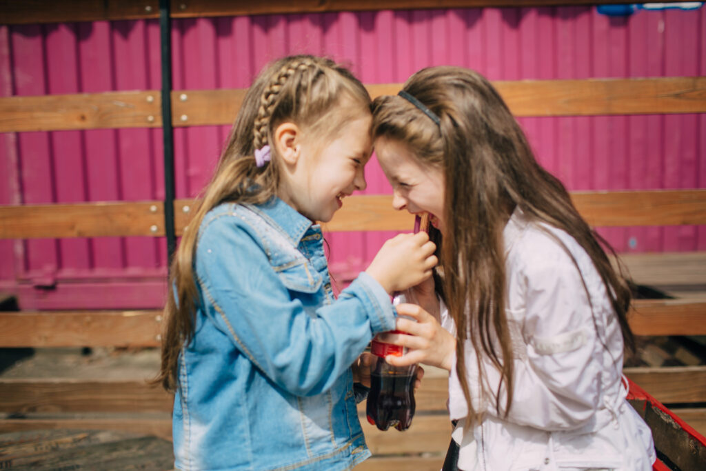 Two girls share a cola in a plastic bottle