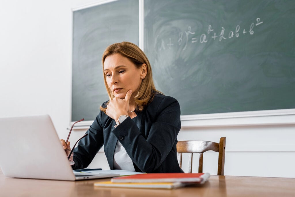 Teacher sits at desk looking at computer with concerned expression