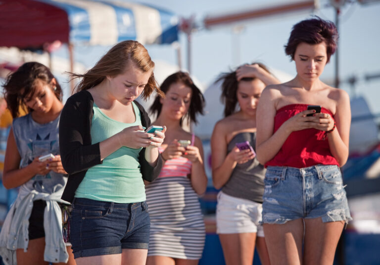 Four young women stand together focused on their phones