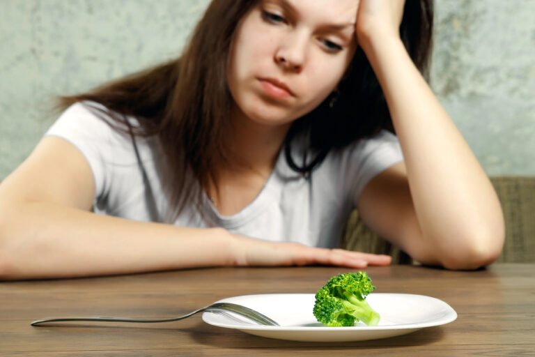 sad young brunette woman dealing with anorexia nervosa or bulimia having small green vegetable on plate. Dieting problems, eating disorder.