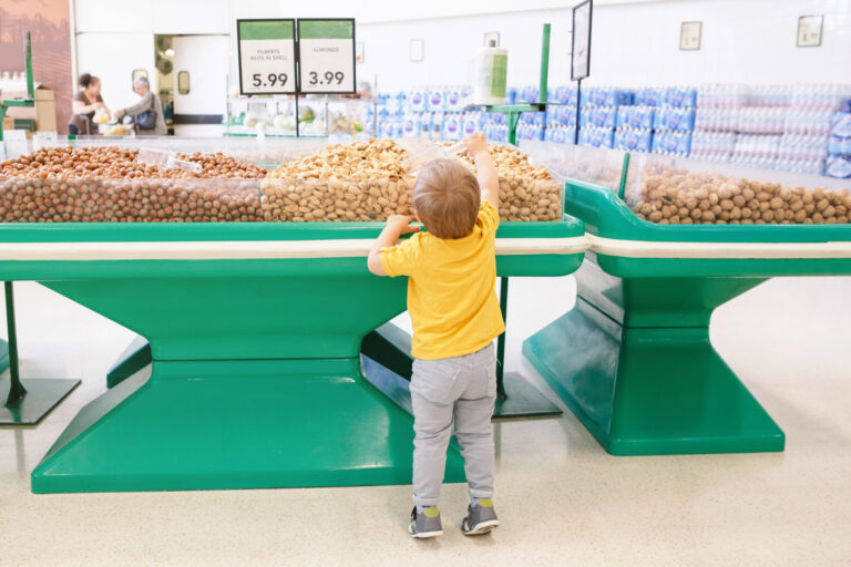 Cute Caucasian baby child choosing nut in supermarket. Funny toddler boy in grocery store packing produce. Healthy tasty summer food snack for kids. Product food allergy concept.