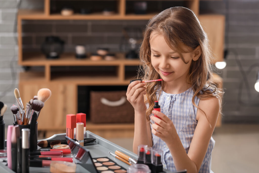 Little girl applies makeup to her face sitting at a table
