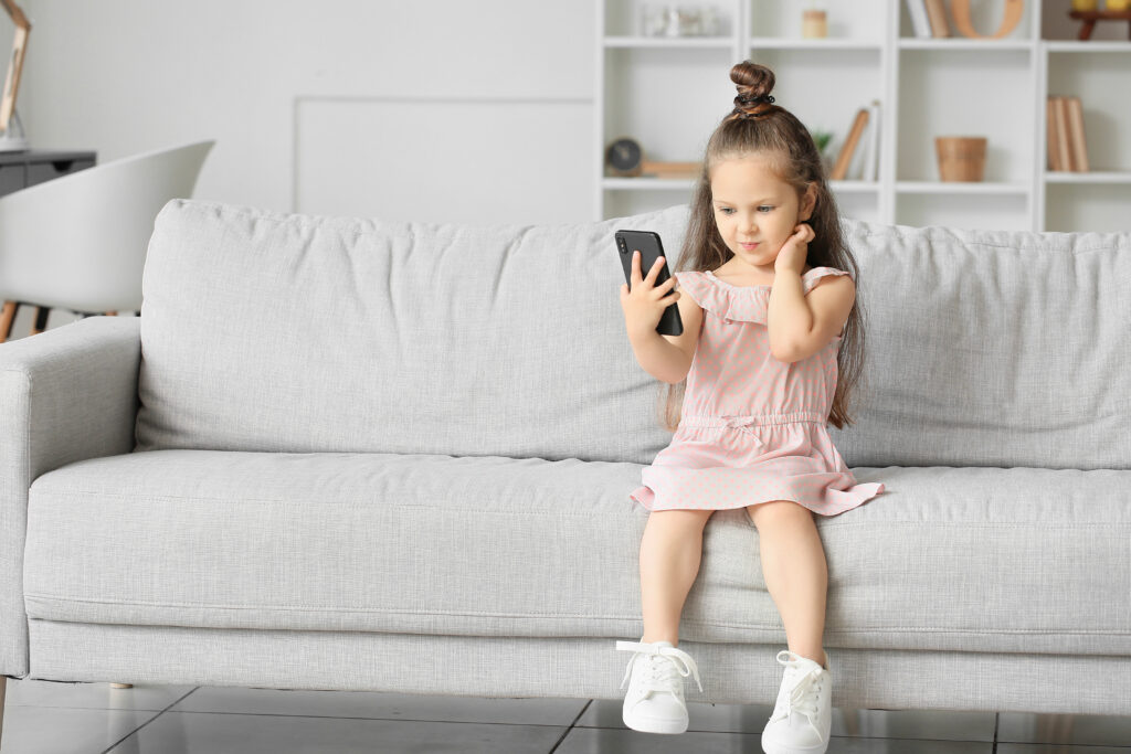 Little girl sitting on sofa playing with cell phone 