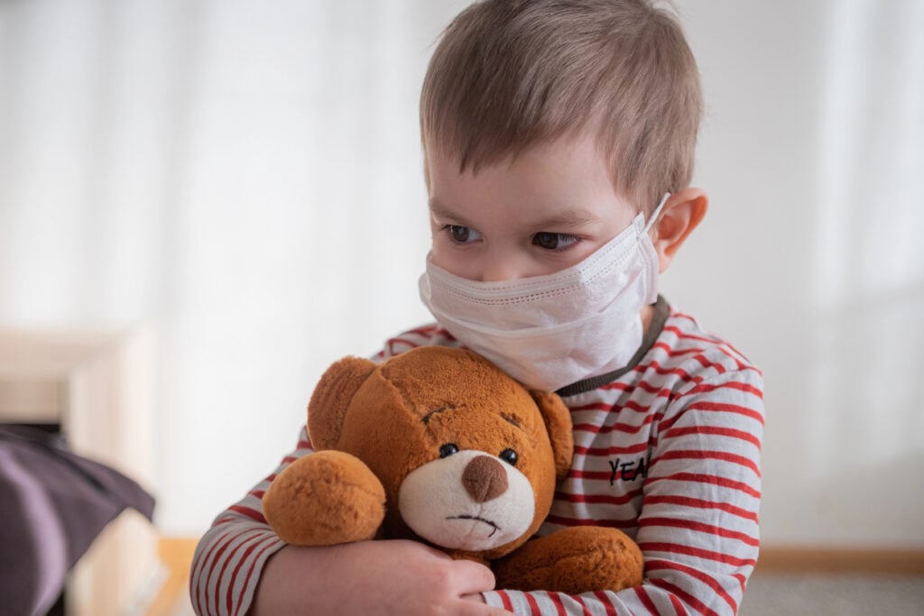 Toddler boy in medical mask embracing his teddy bear. Home isolation coronavirus covid-2019 quarantine
