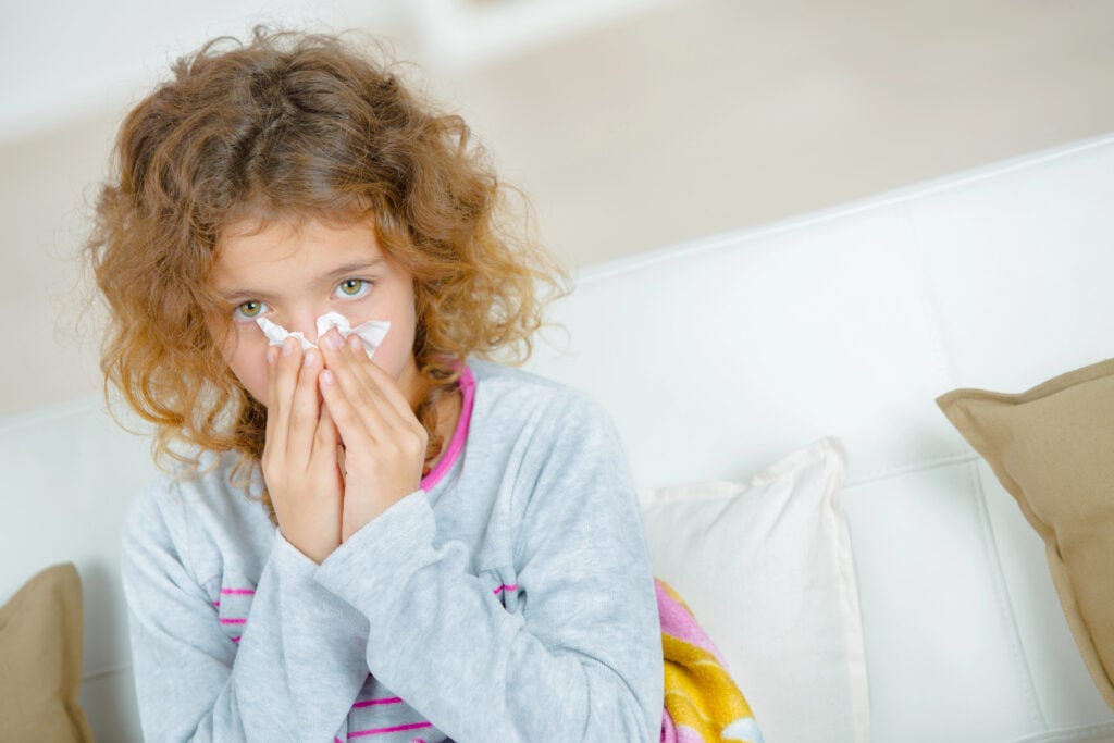 Young girl blowing nose with tissue
