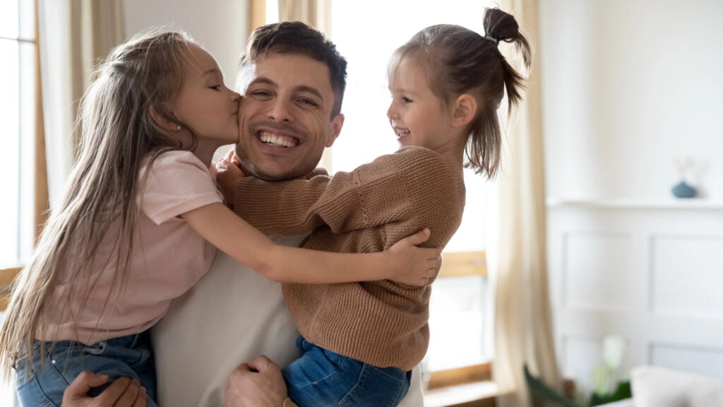 Happy father holding hugging two pretty daughters