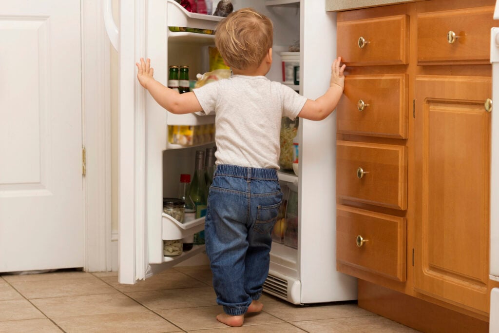 Two years blonde toddler openes fridge and lookes what to eat