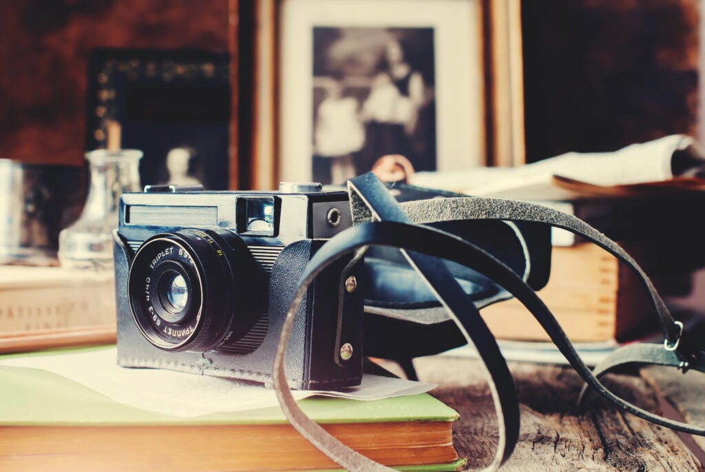 Old Retro Photo Camera with Strap in front of Vintage Things. Toned