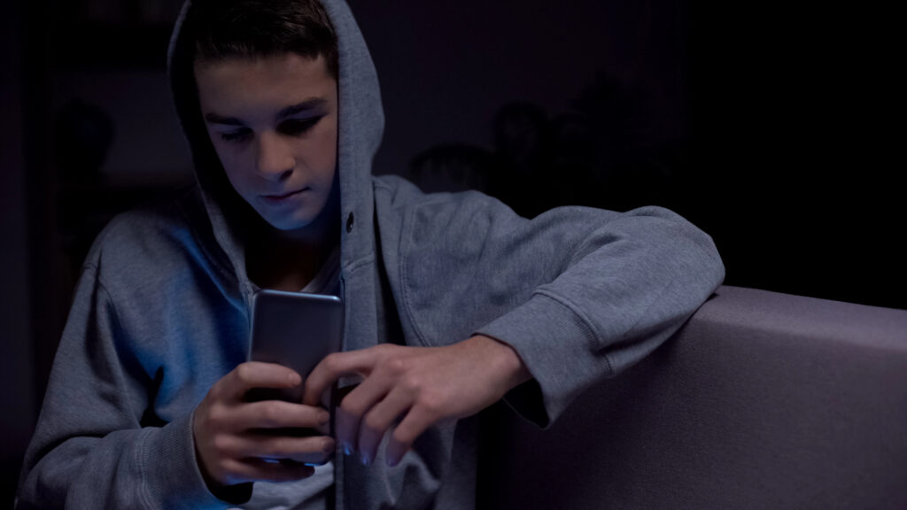 Teen boy playing smartphone late at night instead of sleeping, lack of control