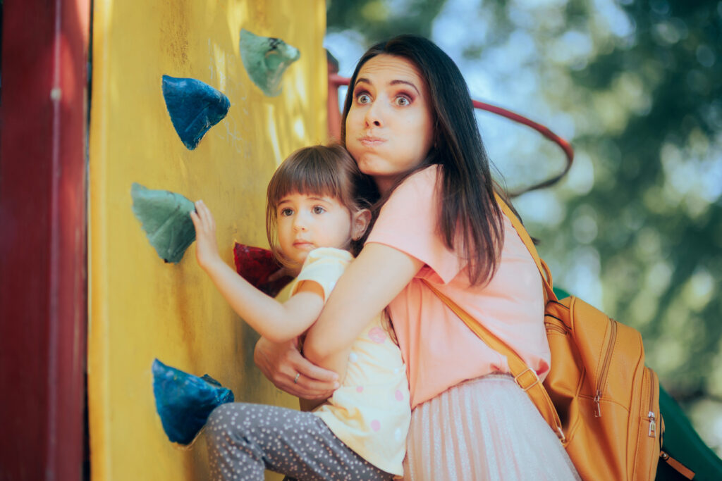 Mom grabs child who is climbing rock wall at playground