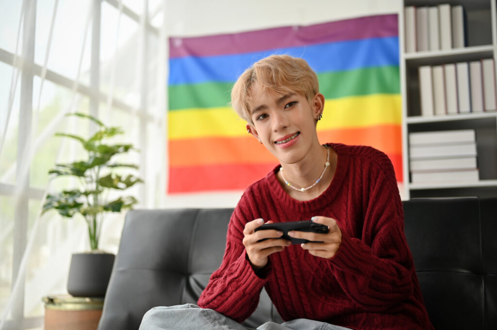 Teen plays video games while rainbow flag hangs in background
