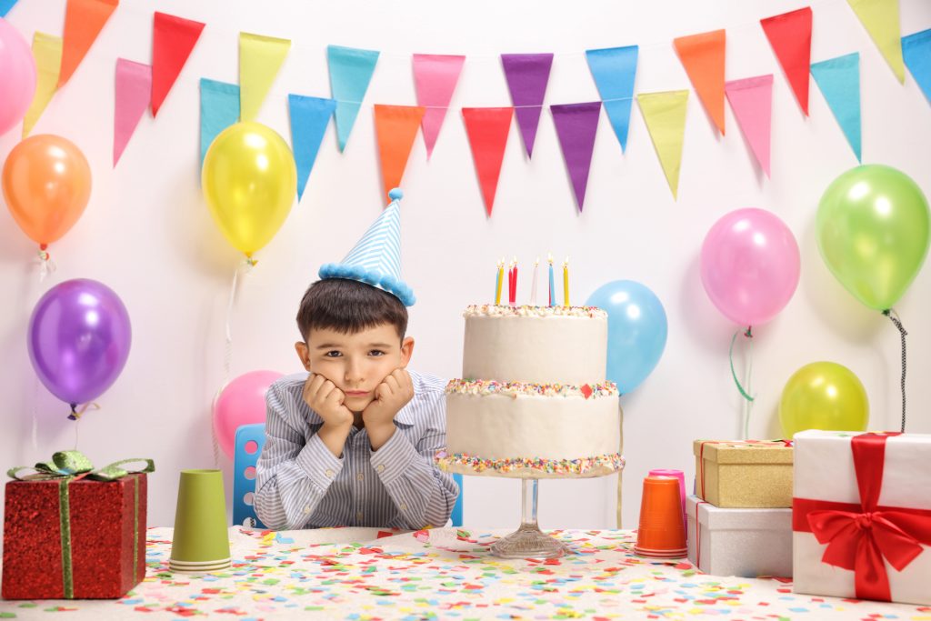 Sad and lonely little boy with a party hat and a birthday cake