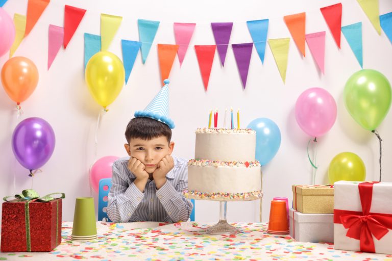 Sad and lonely little boy with a party hat and a birthday cake