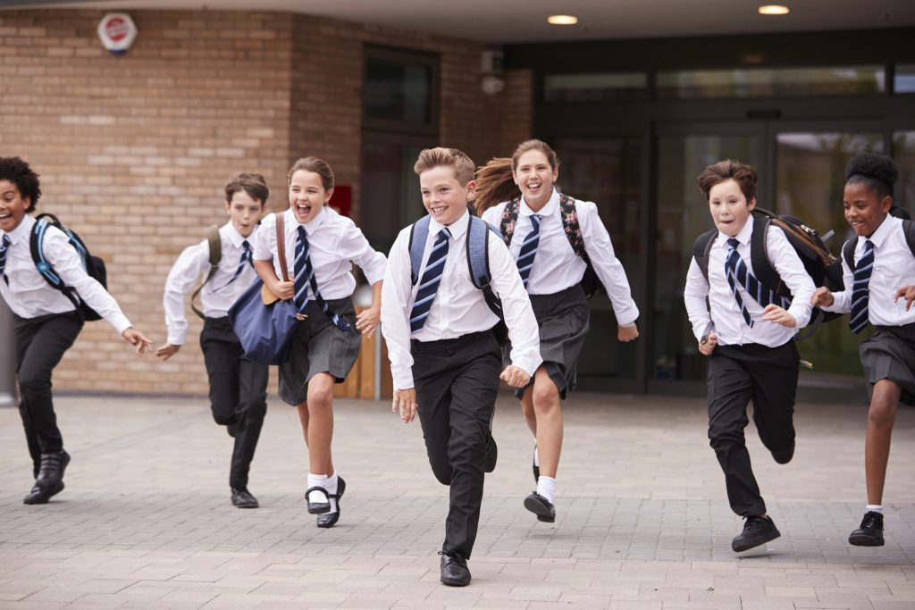 Group Of High School Students Wearing Uniform Running Out Of School Buildings
