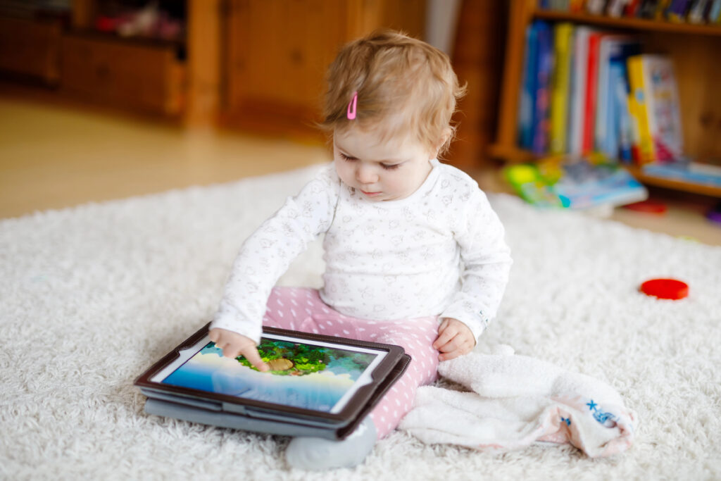 Cute adorable baby girl watching cartoons on tablet pc. Todder child at home touching on screen and playing educational games on computer.