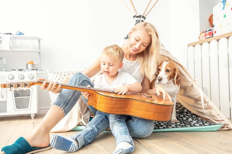 Little boy playing on guitar with mom .